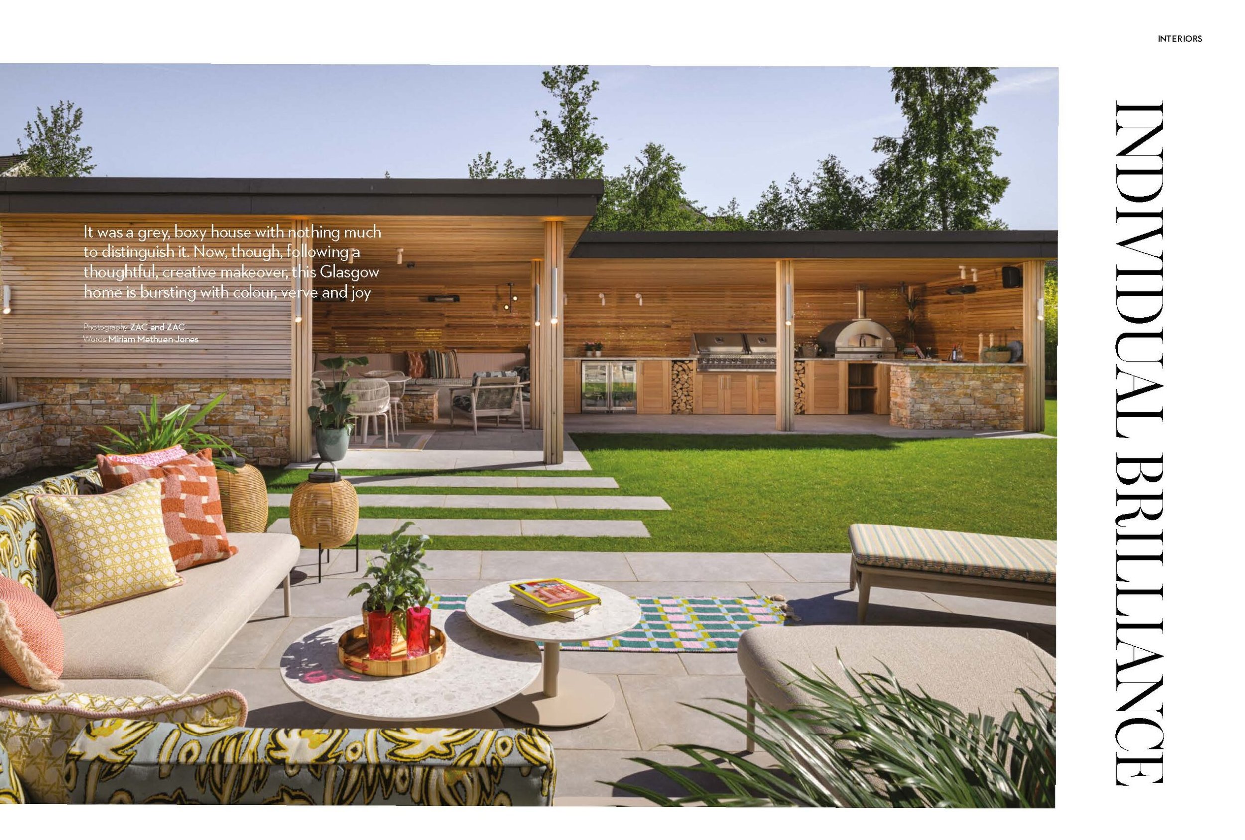 Modern outdoor living area with covered kitchen, pizza oven, dining, vibrant lounge, and a green lawn.
