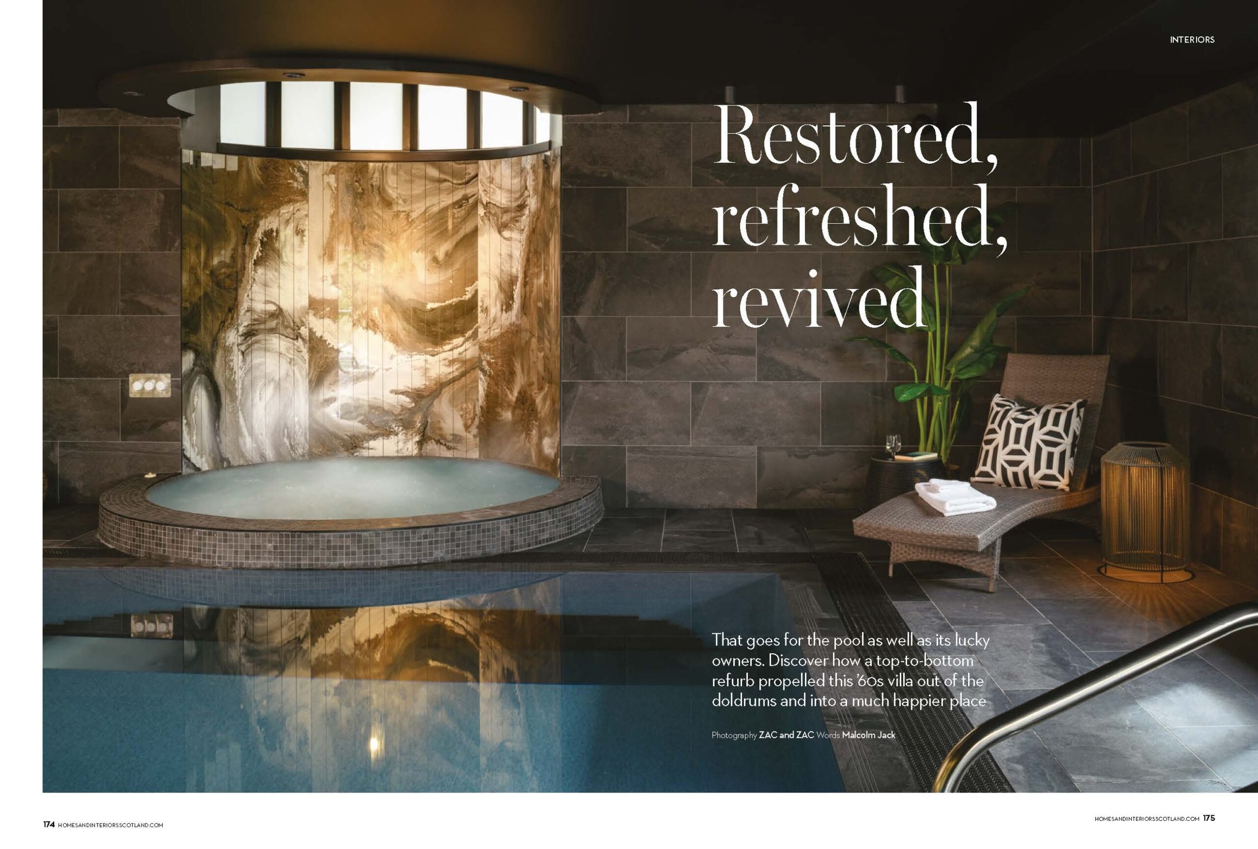 Indoor swimming pool and tiled hot tub with a stunning gold and brown marbled accent wall, lounge chair, and dark stone tiles.
