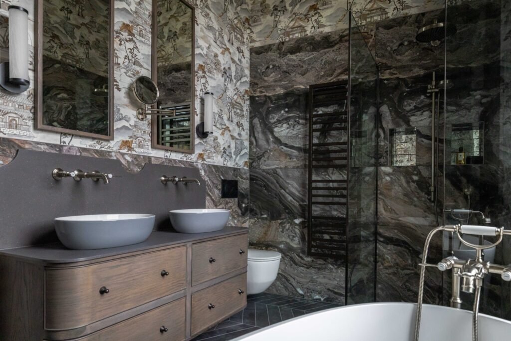 Luxurious bathroom with dark veined marble shower, double vessel sinks, ornate landscape wallpaper, and a freestanding tub.