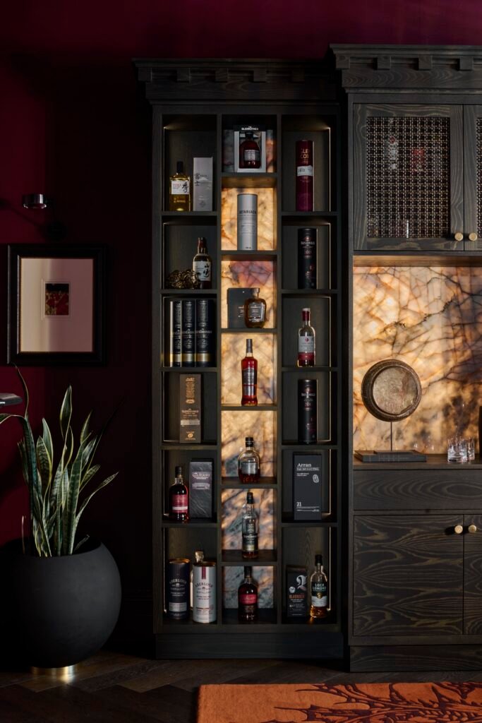 Elegant dark wood liquor cabinet with backlit onyx shelves, whisky collection, snake plant, and deep red walls.