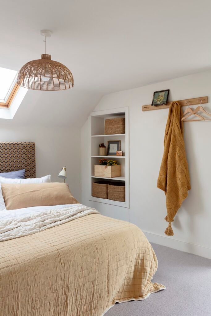 Bright neutral bedroom with skylight, woven pendant light, beige bedding, built-in shelves, and a mustard yellow throw blanket.