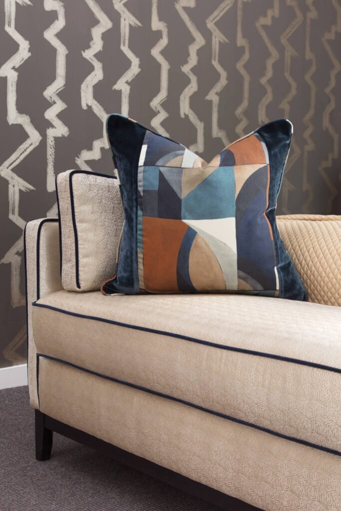Contemporary living room: patterned beige sofa with dark piping, abstract geometric pillow, and zig-zag wallpaper.