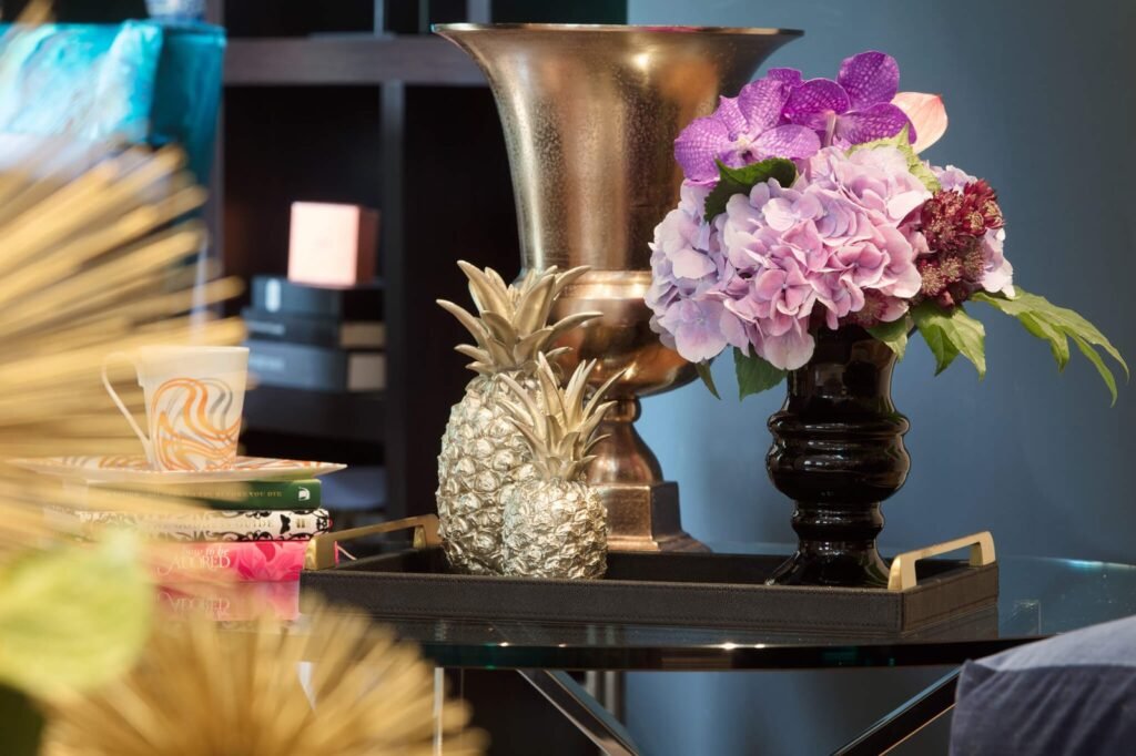 Elegant table decor with purple hydrangeas, gold pineapples, books, and a patterned cup on a black tray.