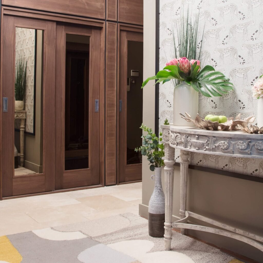 Stylish entryway featuring dark wood sliding doors, an ornate distressed console table, and botanical decorations against patterned wallpaper.