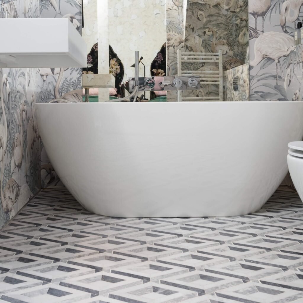 Modern bathroom with white freestanding bathtub, geometric grey and white tiled floor, and flamingo pattern walls.