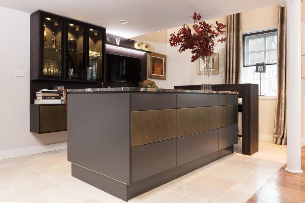 Sleek dark grey kitchen island with bronze accents, marble top, and backlit display cabinets in a contemporary living space.