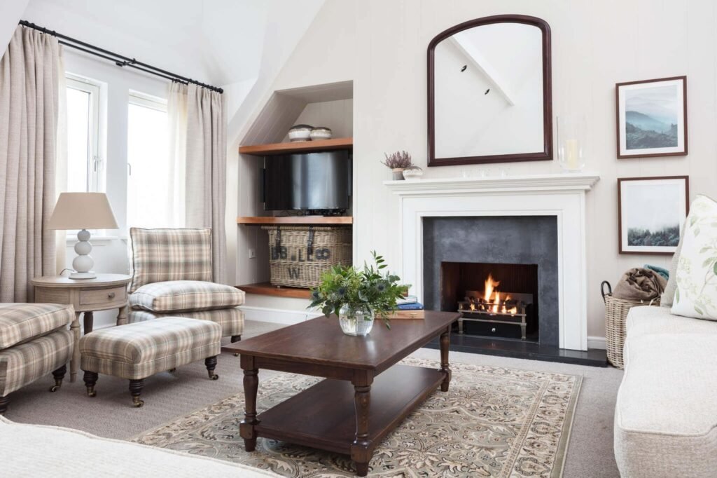 Cozy living room with a lit fireplace, plaid armchairs, wood coffee table, built-in TV, and framed art.