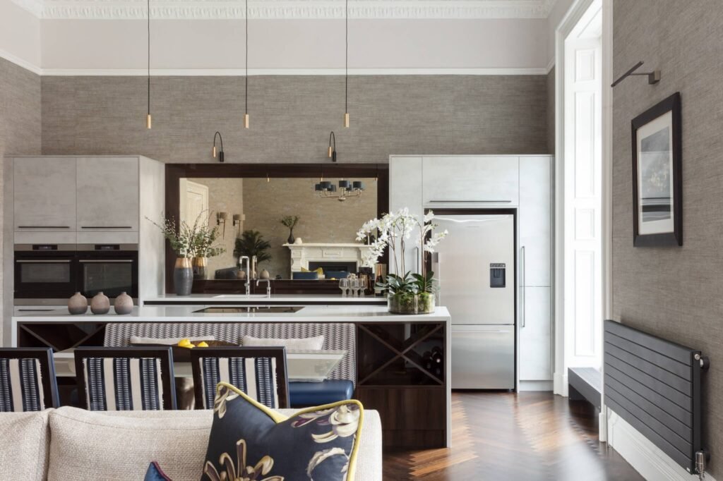 Modern luxury kitchen with an island, integrated appliances, textured walls, and a mirror reflecting a living room fireplace.