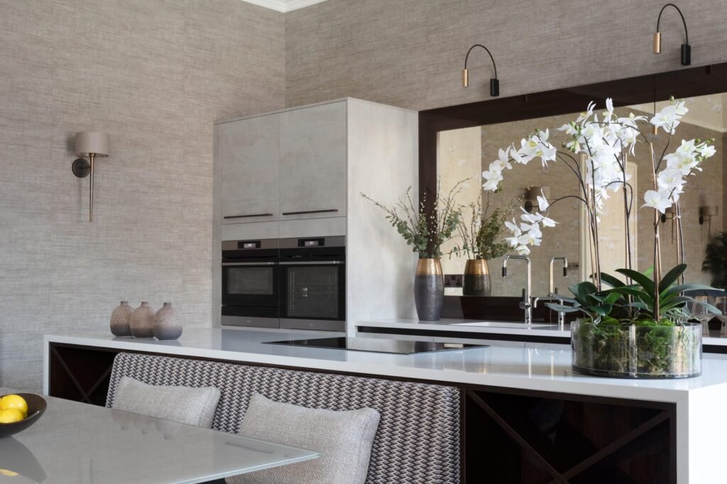 Elegant contemporary kitchen with light grey textured walls, integrated ovens, white countertop island with built-in seating.