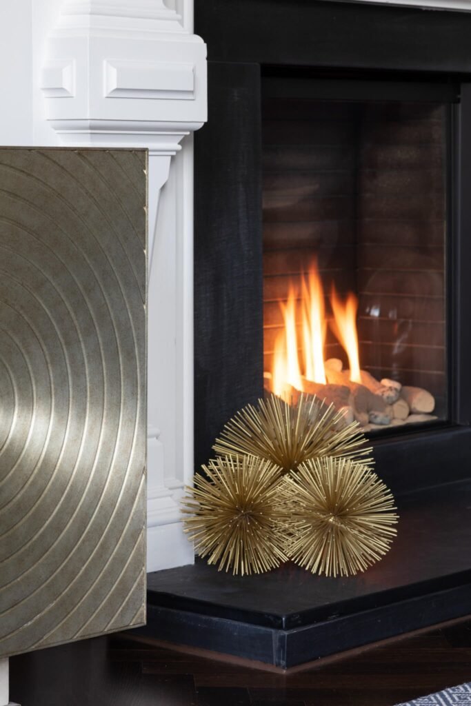 Fireplace with active fire, gold spike balls on black hearth, white mantel, and a silver concentric circle art panel.