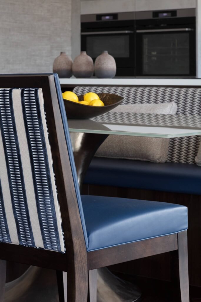 Modern kitchen with dark wood chair, blue leather seat & striped fabric back, navy banquette seating, and built-in ovens.