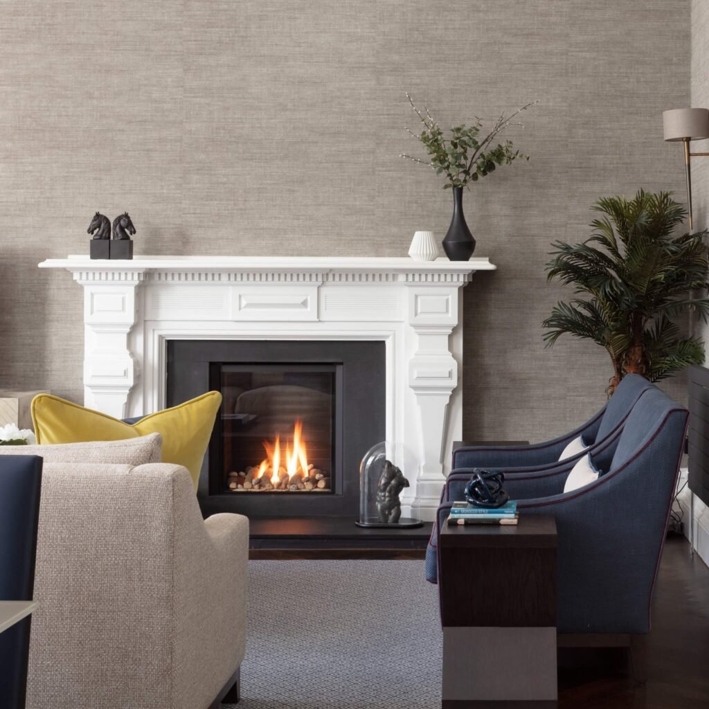 Stylish living room with a lit fireplace, natural textured wallpaper, blue and beige armchairs, and a decorative mantel.