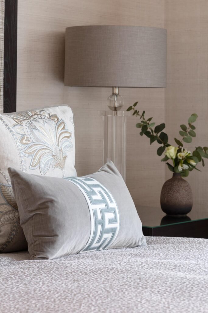 Sophisticated bedroom detail: neutral embroidered and geometric pillows, modern lamp, eucalyptus and white flowers in a vase.