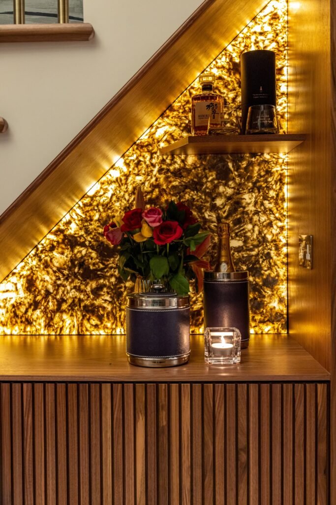 Elegant backlit onyx bar niche with whiskey, champagne, roses, and a candle on a wood fluted cabinet.