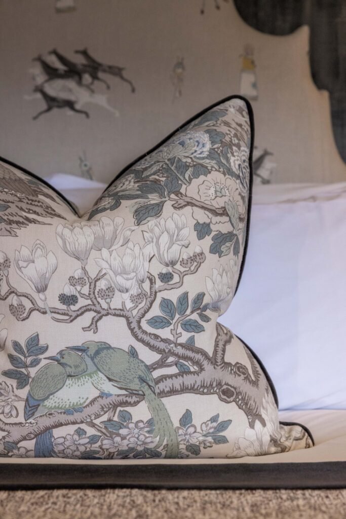Elegant decorative pillow with a detailed pattern of magnolia flowers, muted blue birds on branches, and black piping.
