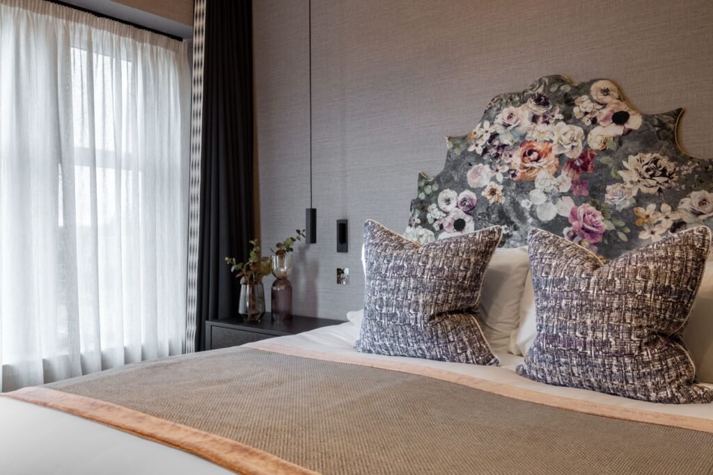 Stylish bedroom featuring a vibrant floral headboard, grey textured walls, modern pendant lights, and patterned throw pillows.