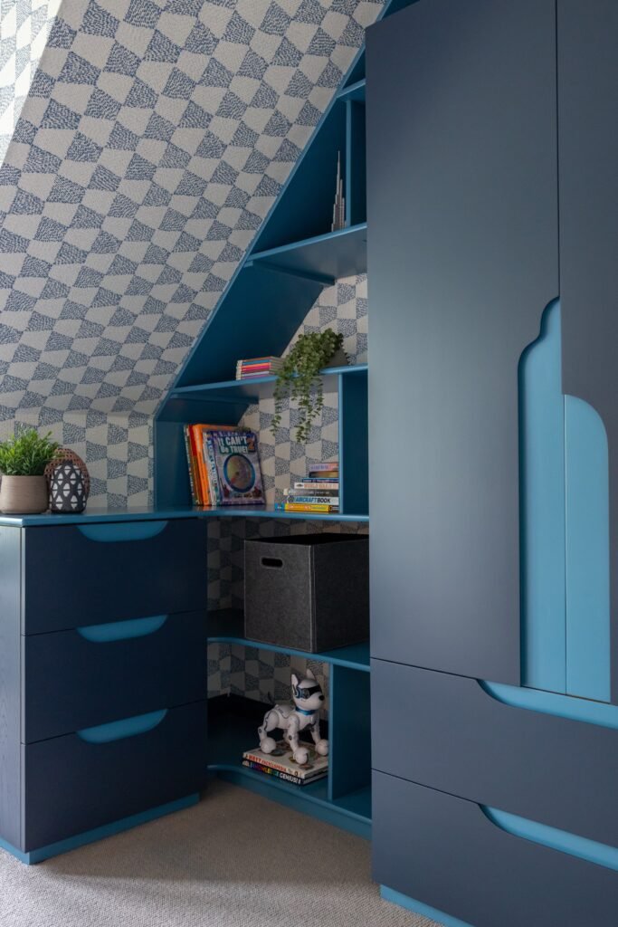 Custom blue built-in storage with drawers, shelves & geometric wallpaper in a modern child's room.