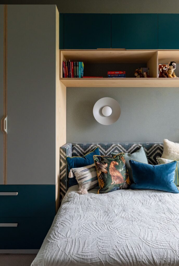 Modern bedroom with grey & teal built-in storage, wood shelves, patterned headboard, and eclectic decorative pillows.