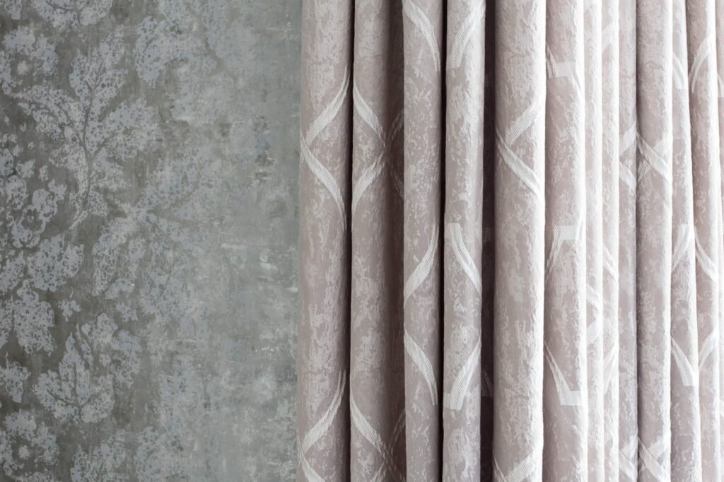 Textured greige curtains with a white geometric pattern against a distressed gray wall featuring a faded floral design.