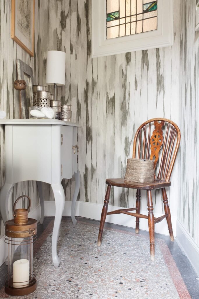 Bohemian entry with grey console, antique wooden chair, textured wallpaper, and terrazzo floor.