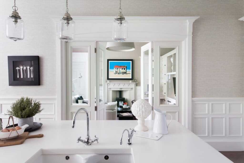 White kitchen island with sink and chrome faucets, opening to a bright living room featuring a fireplace and colorful art.