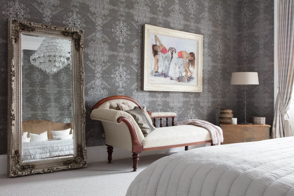 Luxurious bedroom with intricate gray damask wallpaper, large ornate silver mirror, elegant chaise lounge, and ballet art.