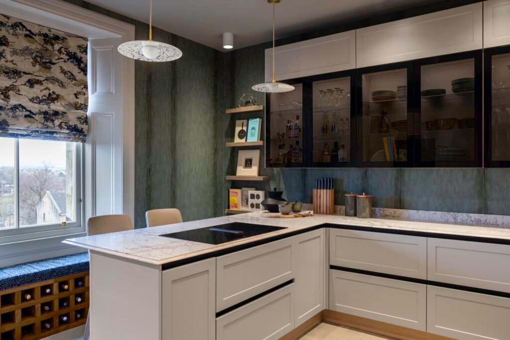 Elegant kitchen with green textured walls, white cabinetry, quartz island with cooktop, glass display uppers, and window seat with wine storage.