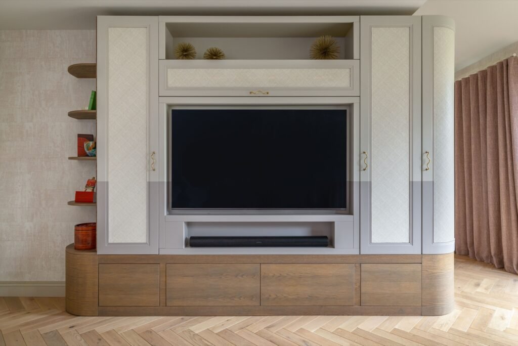Elegant built-in media center with TV, soundbar, light grey textured cabinets, wood storage, and open side shelves.