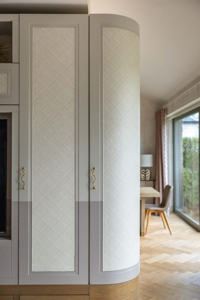 Tall grey custom cabinets with textured panels and wavy gold handles; curved end shows dining area with wood floor.