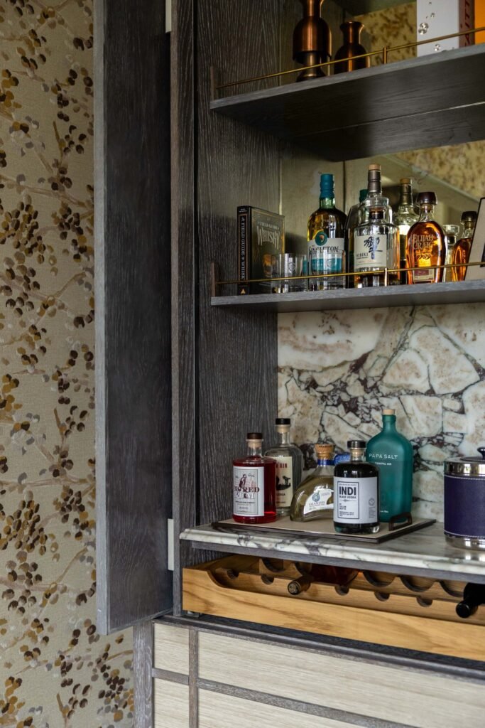 Luxurious dark wood built-in bar cabinet with marble backsplash, liquor bottles, glasses, and a wine rack.