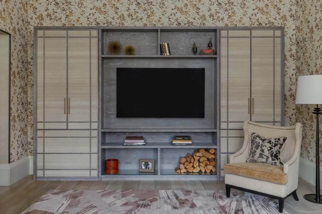 Inviting living room with custom light wood and gray built-in media cabinet, patterned wallpaper, and cozy armchair.