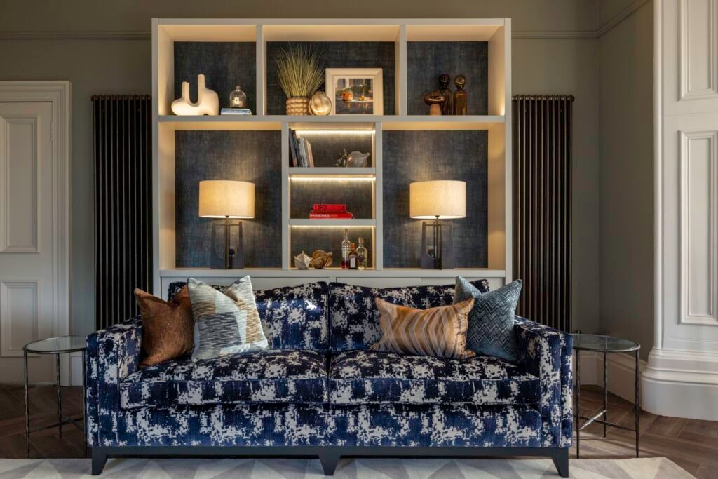 Stylish living room with a navy patterned sofa and a striking backlit built-in shelving unit filled with decor.