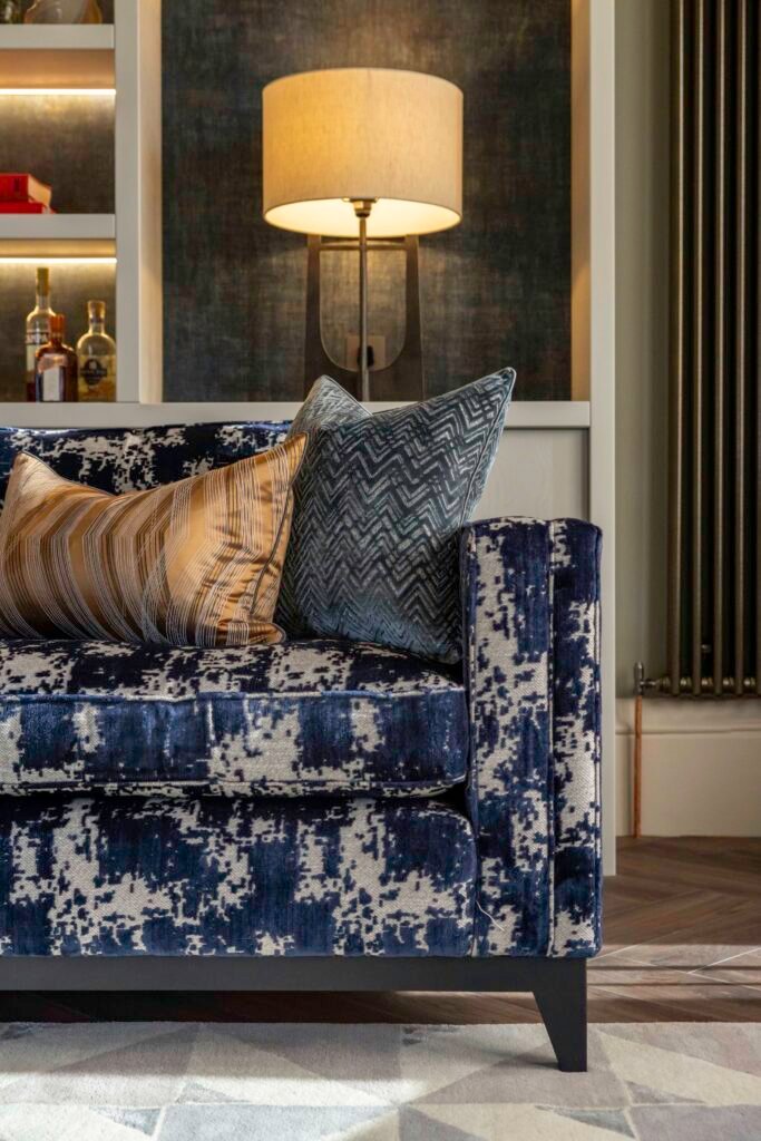 Modern interior with a blue abstract patterned sofa, gold and teal throw pillows, and a glowing table lamp.