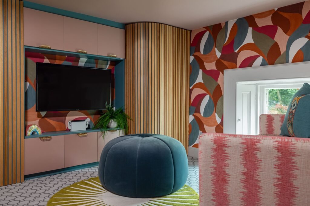 Modern living room with abstract patterned wallpaper, blush media console, wood slats, teal pouf, and hexagon floor tiles.