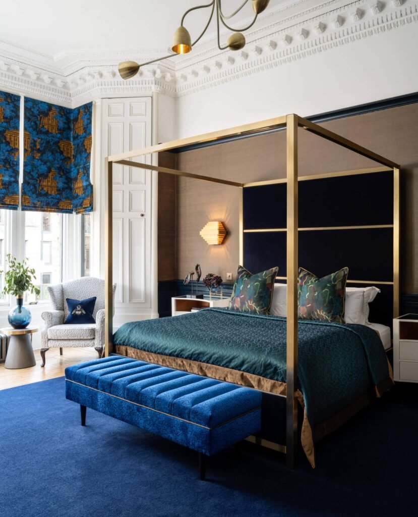 Luxurious blue & gold bedroom: four-poster bed, velvet headboard, patterned window blinds, ornate ceiling molding.