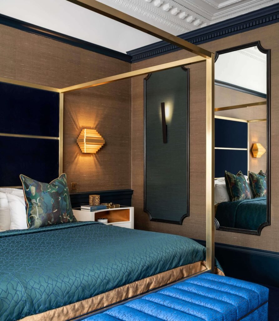 Elegant bedroom with a gold four-poster bed, teal bedding, rich brown textured walls, and striking wall sconces.
