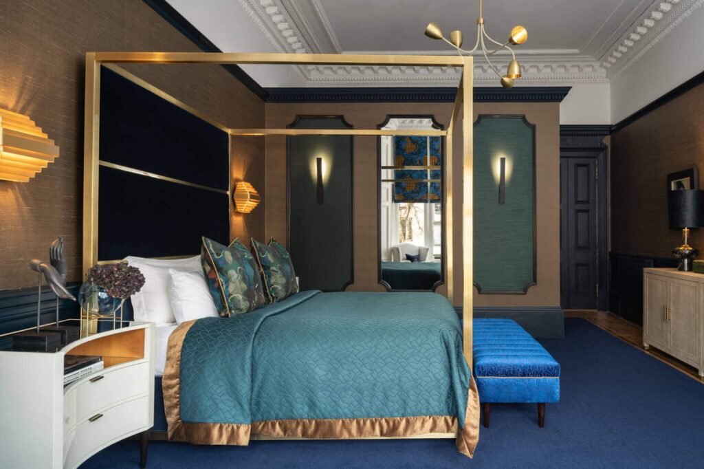 Luxurious bedroom with brass four-poster bed, teal quilt, blue carpet, ornate ceiling, and rich blue & brown walls.