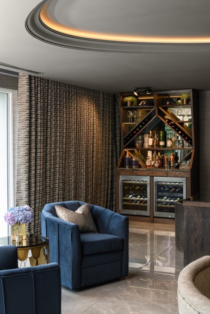 Luxurious modern living room with a custom bar, two blue armchairs, marble floor, and decorative ceiling lights.