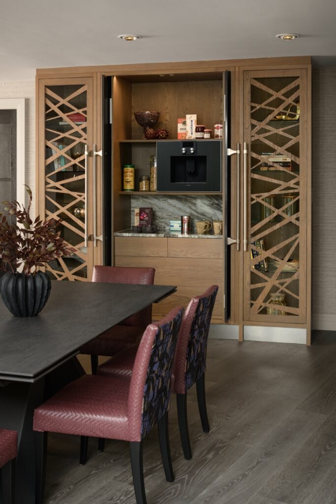 Modern dining area featuring a custom wood coffee bar with a marble backsplash, lattice-front cabinets, and maroon chairs.