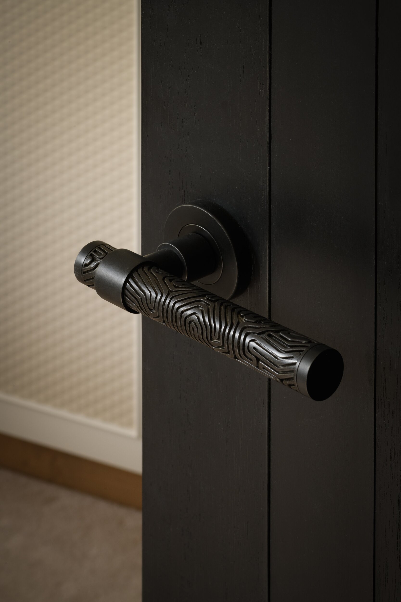 Matte black door handle with intricate, wavy topographic texture, mounted on a dark wood door.