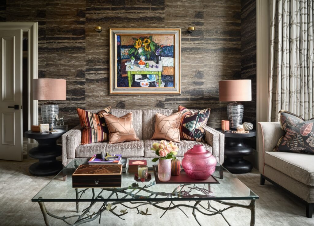 Glamorous living room featuring a velvet sofa, still life painting, textured brown wallpaper, and a glass coffee table with branch base.