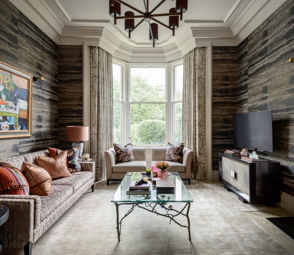 Elegant living room with dark textured walls, large bay window, plush sofas, unique branch-base coffee table, and modern chandelier.