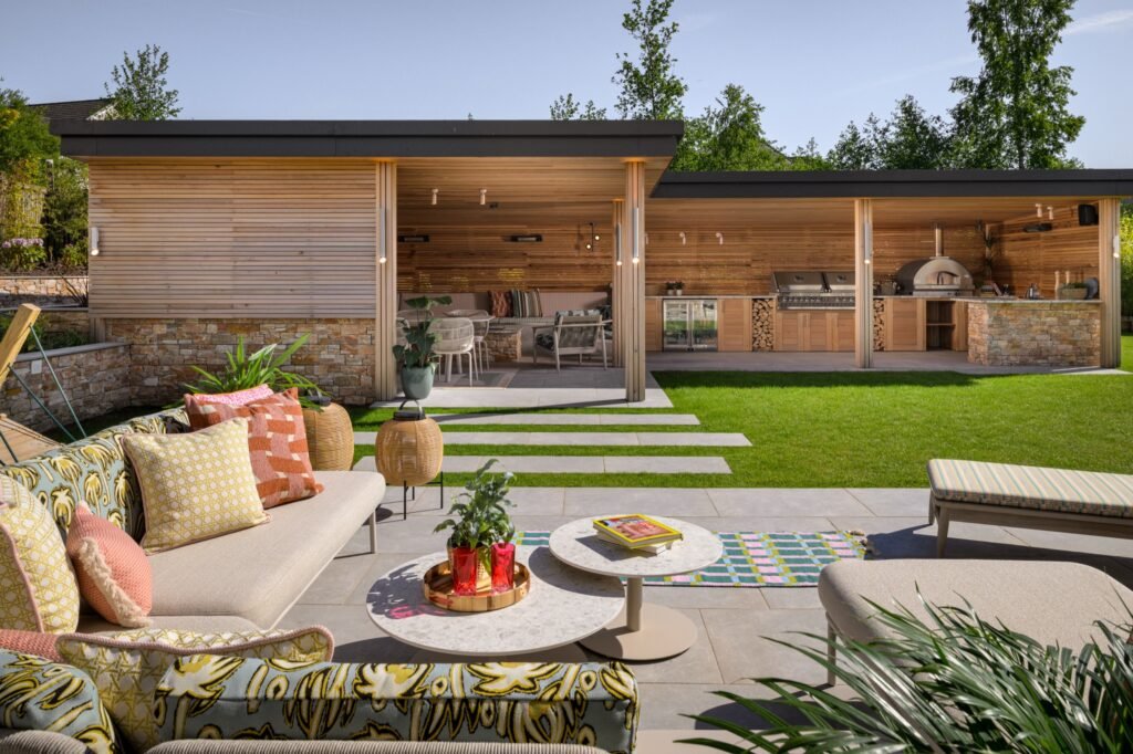 Lush backyard with a contemporary wood-and-stone outdoor kitchen and dining pavilion, plus a comfortable lounge area and green lawn.