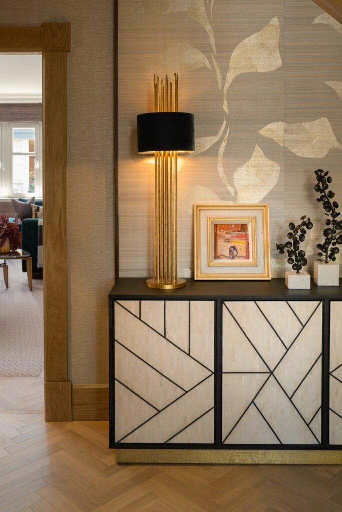 Elegant modern interior with a geometric console, gold lamp, framed art, and black decorative branches against botanical wallpaper.