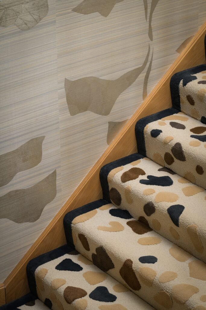 Modern staircase with a textured carpet runner featuring cream, brown, and black organic shapes, alongside a subtly patterned wall.
