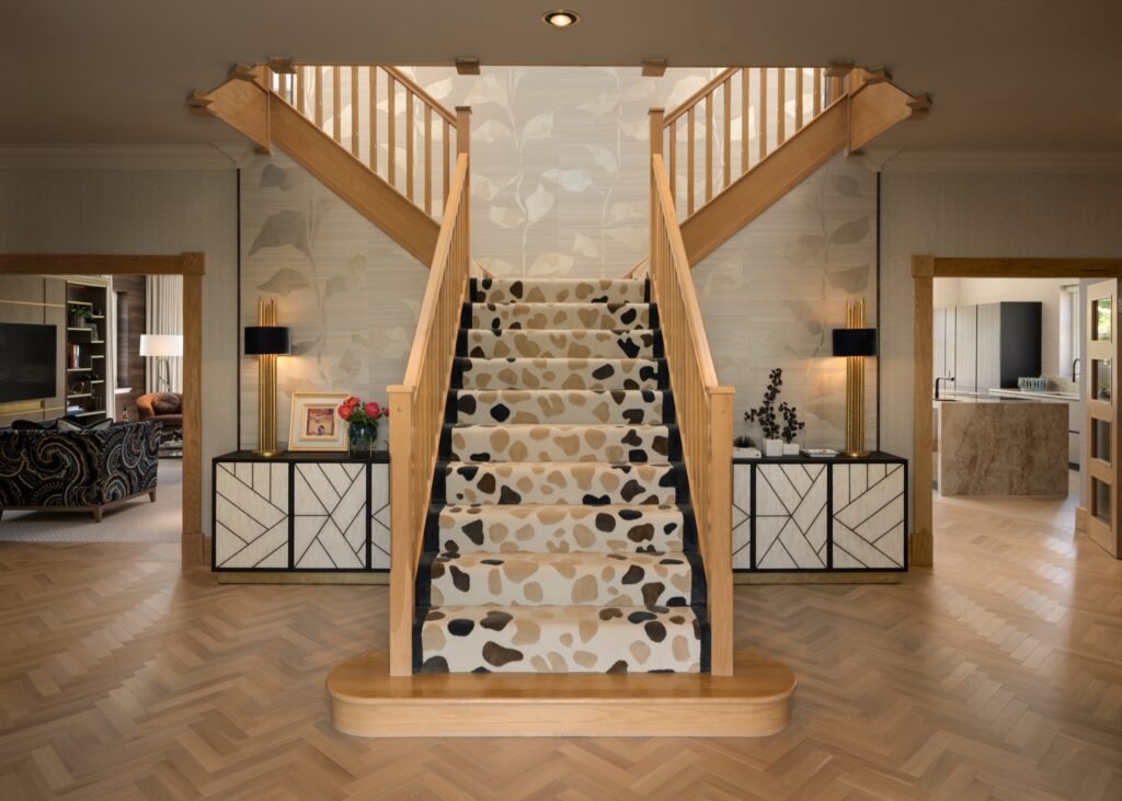 Modern grand foyer with light wood split staircase, abstract animal print carpet runner, herringbone floor, and patterned sideboards.