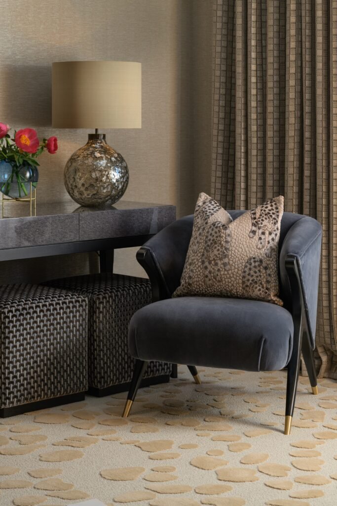 Luxurious seating area with dark grey velvet armchair, animal print pillow, shimmering lamp, geometric curtains, and abstract rug.