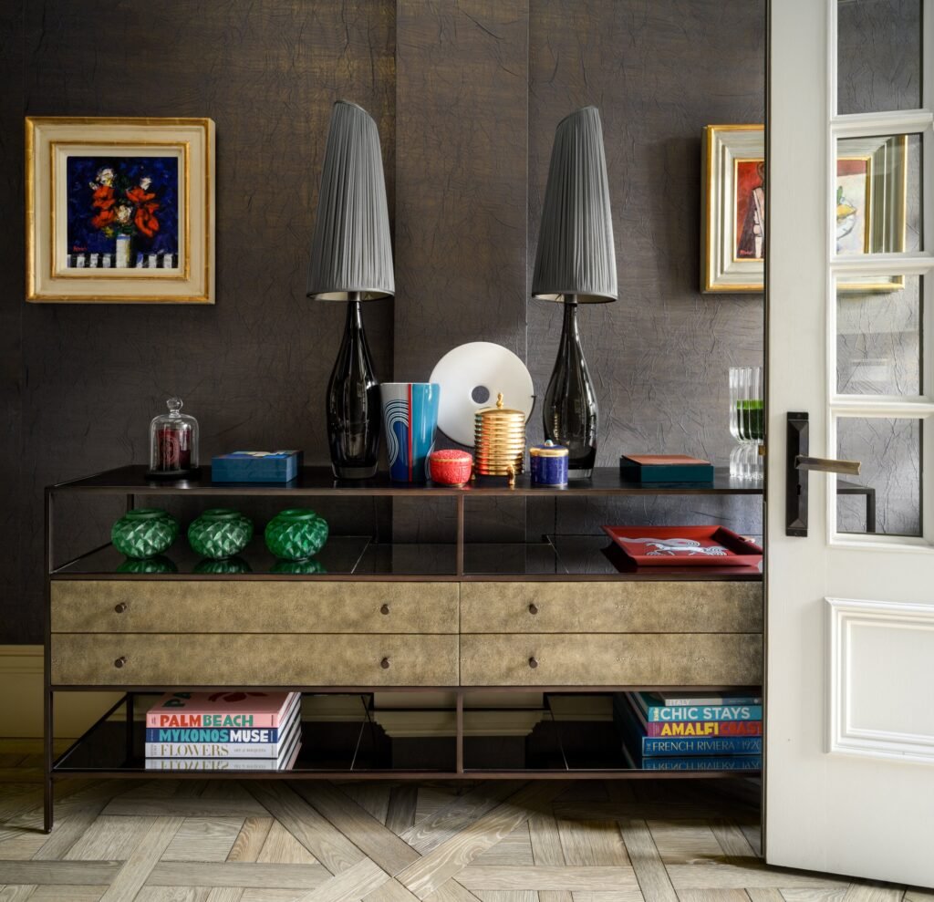 Elegant console with black lamps, art, decor against textured walls, and a patterned wood floor in a refined interior.