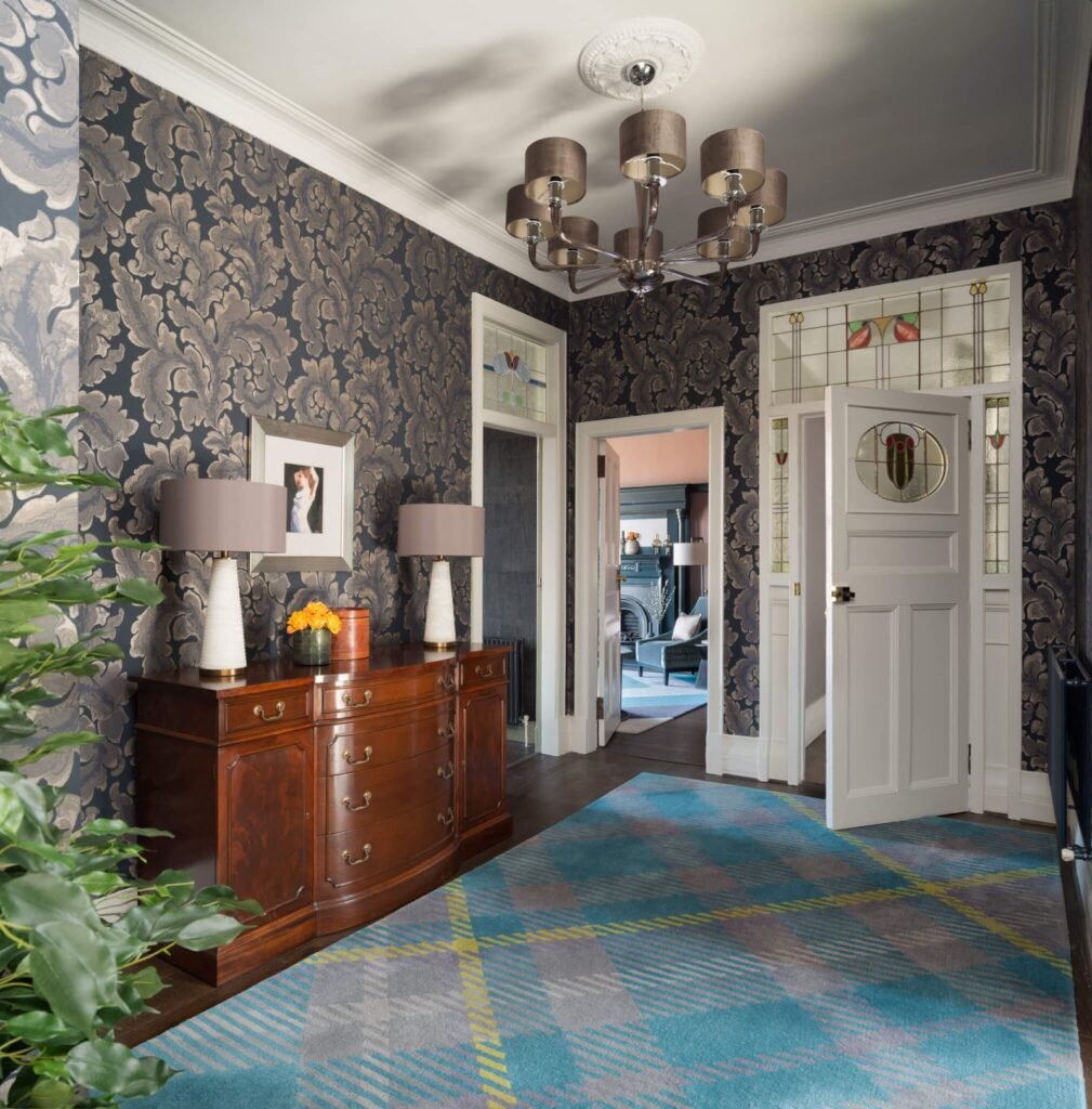 Sophisticated entryway with dark damask wallpaper, antique wood console, stained glass doors, and a vibrant blue plaid rug.