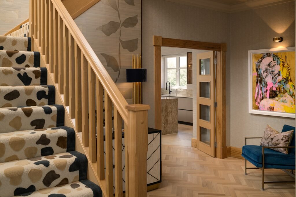 Stylish entryway with a light oak staircase, cow print runner, herringbone floor, vibrant abstract art, and teal armchair.